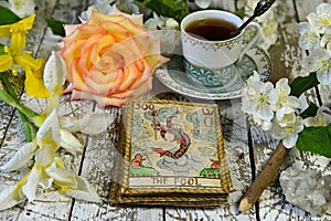 Tarot card Joker with rose and lily flowers on witch altar, fortune telling seance photo