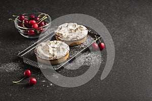 Tart with cherry filling with cocoa cream on a black plate with cherry berries on a dark background