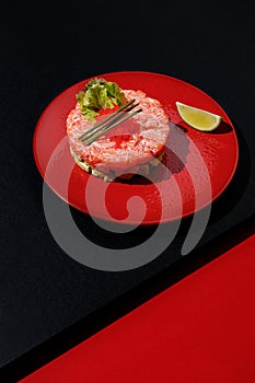 Tartar with salmon and caviar with lime at red color plate at black and red background with sunlight and shadows, minimalism,top