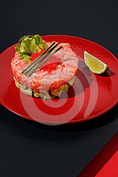 Tartar with salmon and caviar with lime at red color plate at black and red background with sunlight and shadows, minimalism,top