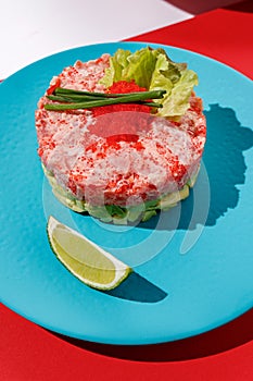 Tartar with tuna and caviar with lime at blue pastel color plate at blue at red background with sunlight and shadows, minimalism,