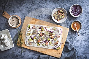 Tarte flambee with rhubarb, red onions, goat cheese and honey, prepared for baking, gray background