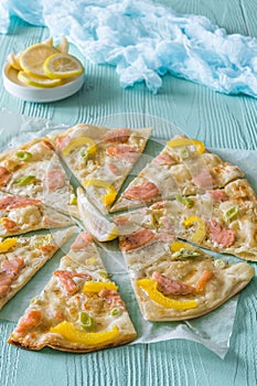 Tarte flambee with salmon, yellow pepper and spring onions on light blue background
