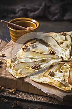 Tarte flambee witgh pear, goat cheese, honey and walnuts on dark rustic wooden background