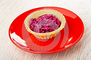 Tartlet with beetroot salad in red saucer on table