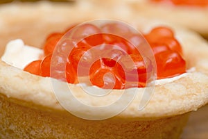 The tartlet with red caviar and butter on wooden brown table macro view