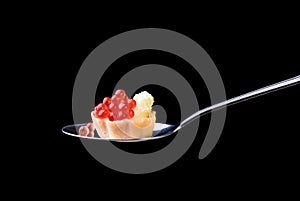 Tartlet with red caviar on a tablespoon on a black background