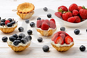 Tartlets with cream, blueberries, raspberries and strawberries on white wooden table. Selective focus.