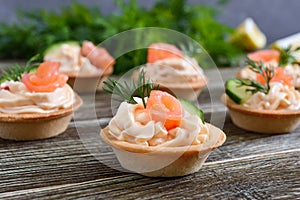 Tartlets with cream cheese and salted salmon on a wooden background. Tasty light snack for a party.