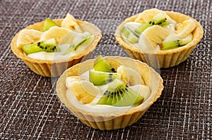 Tartlets with slices of kiwi, banana and yogurt on mat