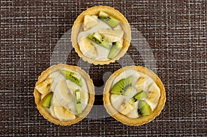 Tartlets with slices of kiwi, banana and yogurt on mat. Top view