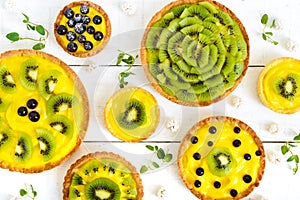 Tartlets, tartas from custard, kiwi and black currant of different sizes on a white wooden background photo