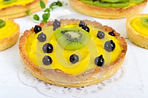 Tartlets, tartas from custard, kiwi and black currant on a white wooden background. photo