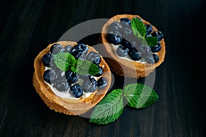 Tarts with blueberries and mint on dark wood background