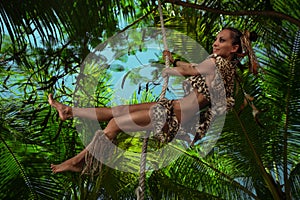 Tarzan wearing in leopard fur swinging on a rope with a parrot in jungle