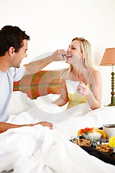 Taste this...A happy young couple enjoying breakfast together in bed at home.
