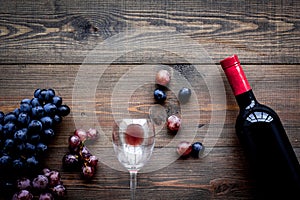 Taste red wine. Bottle of red wine, glass and black grape on dark wooden background top view copyspace