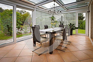 A tastefully furnished winter garden there is a dining table decorated with yellow tulips