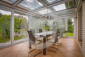 a tastefully furnished winter garden there is a dining table decorated with yellow tulips