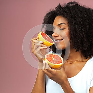 Tastes good and smells divine. Studio shot of an attractive young woman eating grapefruit against a pink background.