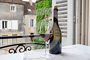 Tasting of burgundy red wine from grand cru pinot noir  vineyards, glass and bottle of wine and view on old town street in
