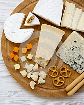 Tasting cheese with bread sticks, walnuts and pretzels on bamboo board over white wooden background, top view. Food for wine. From