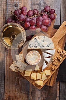 Tasting cheese dish on a wooden plate. Food for wine and romantic, cheese delicatessen on a wooden rustic table. Top view