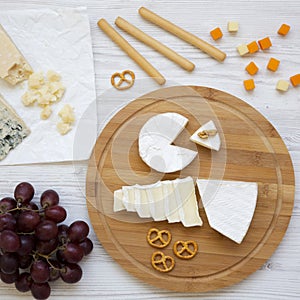 Tasting cheese with grapes, bread sticks, walnuts and pretzels over white wooden background, top view. Food for wine. Flat lay.