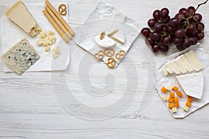 Tasting cheese with grapes, bread sticks, walnuts and pretzels on wooden background, top view. Food for romantic. Flat lay.