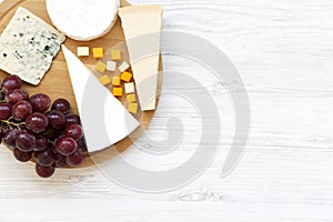 Tasting cheese with grapes on white wooden background. Food for wine, top view. Space for text.