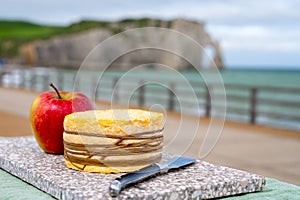 Tasting of yellow livarot cow cheese from Calvados region served with apple and view on alebaster cliffs Porte d`Aval in Etretat,