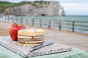 Tasting of yellow livarot cow cheese from Calvados region served with apple and view on alebaster cliffs Porte d`Aval in Etretat,