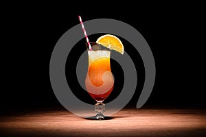 tasty alcohol cocktail with orange juice, orange slice and drinking straw on table
