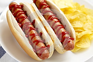 Tasty American Hot Dog with Potato Chips on a white plate, low angle view. Close-up