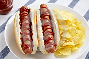 Tasty American Hot Dog with Potato Chips on a white plate, side view. Close-up