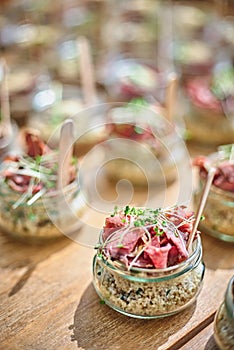 Tasty appetizers with wooden spoons served in glass jars on wooden table.