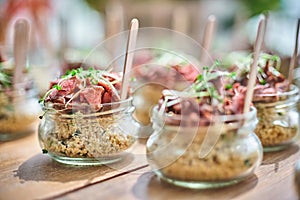 Tasty appetizers with wooden spoons served in glass jars on wooden table.