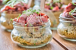 Tasty appetizers with wooden spoons served in glass jars on wooden table.