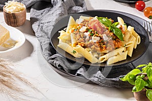 Tasty appetizing classic italian penne pasta with vegetarian lentil bolognese sauce, cheese parmesan and basil on plate on light