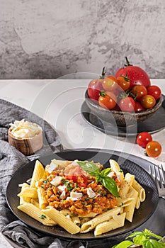 Tasty appetizing classic italian penne pasta with vegetarian lentil bolognese sauce, cheese parmesan and basil on plate on light