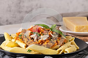 Tasty appetizing classic italian penne pasta with vegetarian lentil bolognese sauce, cheese parmesan and basil on plate on light