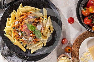 Tasty appetizing classic italian penne pasta with vegetarian lentil bolognese sauce, cheese parmesan and basil on plate on light