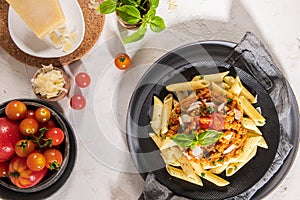 Tasty appetizing classic italian penne pasta with vegetarian lentil bolognese sauce, cheese parmesan and basil on plate on light