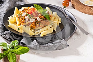 Tasty appetizing classic italian penne pasta with vegetarian lentil bolognese sauce, cheese parmesan and basil on plate on light