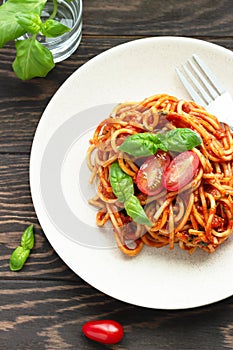 Tasty appetizing classic italian spaghetti pasta with tomato sauce, fresh cherry tomatoes and basil on ceramic plate.