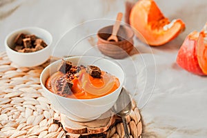 Tasty appetizing pumpkin creamy soup decorated with chili flakes pepper served in white bowl on autumn comfort background concept