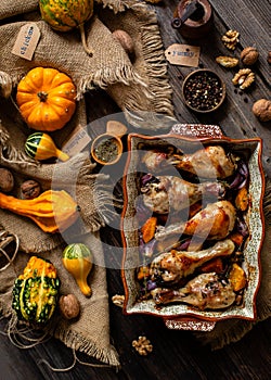 Tasty baked chicken drumsticks with pumpkin and red onion slices in baking ceramic pan