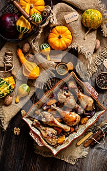 Tasty baked chicken drumsticks with pumpkin and red onion slices in baking ceramic pan