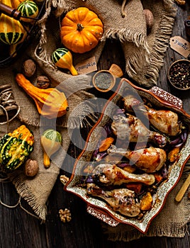 Tasty baked chicken drumsticks with pumpkin and red onion slices in baking ceramic pan