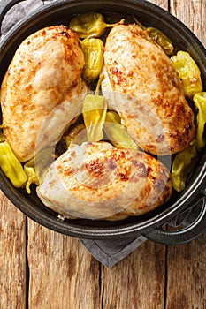 Tasty baked chicken fillet with peperoncini peppers close-up in a pan on the table. vertical top view